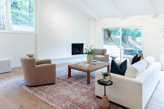 living room with lofted ceiling with beams, a brick fireplace, a healthy amount of sunlight, and light hardwood / wood-style floors