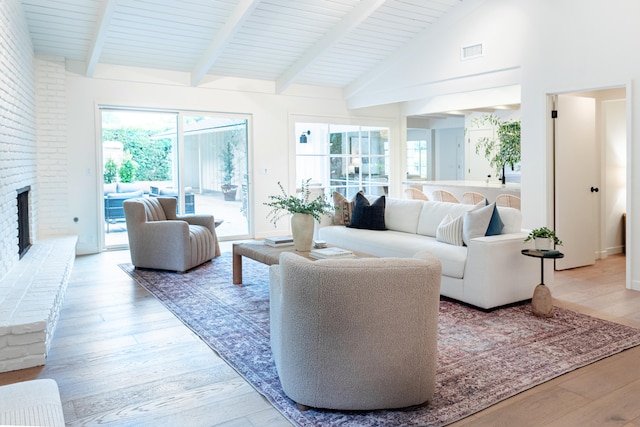 living room featuring light wood-type flooring, high vaulted ceiling, beam ceiling, and a brick fireplace