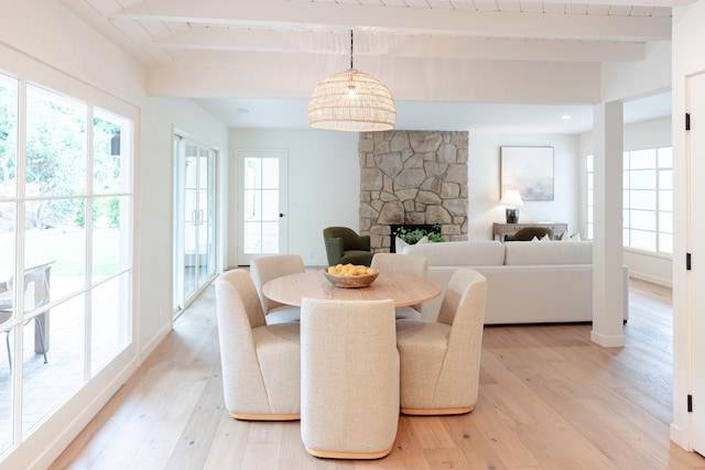 dining space featuring light wood-type flooring, beam ceiling, and a stone fireplace