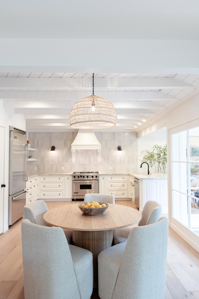 dining area with light hardwood / wood-style floors, beam ceiling, and sink