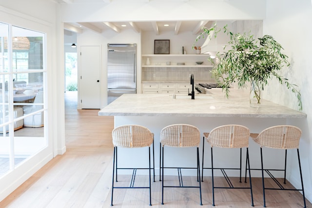 kitchen with stainless steel built in fridge, a kitchen bar, kitchen peninsula, beam ceiling, and light hardwood / wood-style floors