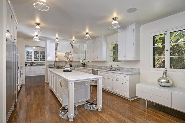 kitchen with a center island, custom exhaust hood, dark hardwood / wood-style flooring, white cabinetry, and a breakfast bar area