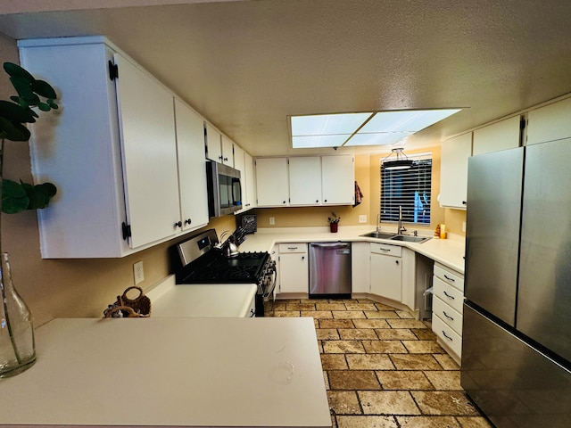 kitchen with white cabinets, a skylight, appliances with stainless steel finishes, sink, and a textured ceiling