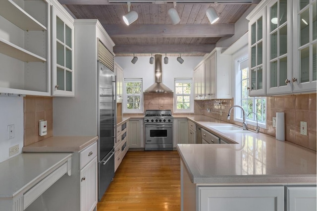 kitchen featuring high end appliances, beamed ceiling, tasteful backsplash, and wall chimney range hood