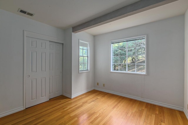 unfurnished bedroom with light wood-type flooring, a closet, and beamed ceiling