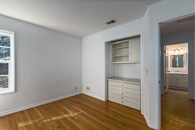 unfurnished bedroom featuring multiple windows, wood-type flooring, ensuite bathroom, and sink