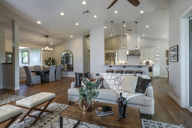 living room with ceiling fan with notable chandelier, high vaulted ceiling, and hardwood / wood-style flooring