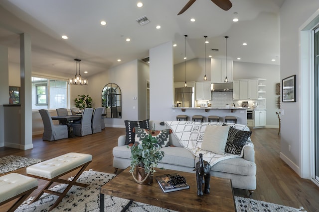 living room featuring ceiling fan with notable chandelier, high vaulted ceiling, wood finished floors, and visible vents