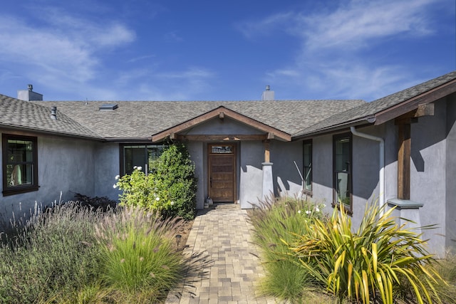 entrance to property featuring roof with shingles, a chimney, and stucco siding