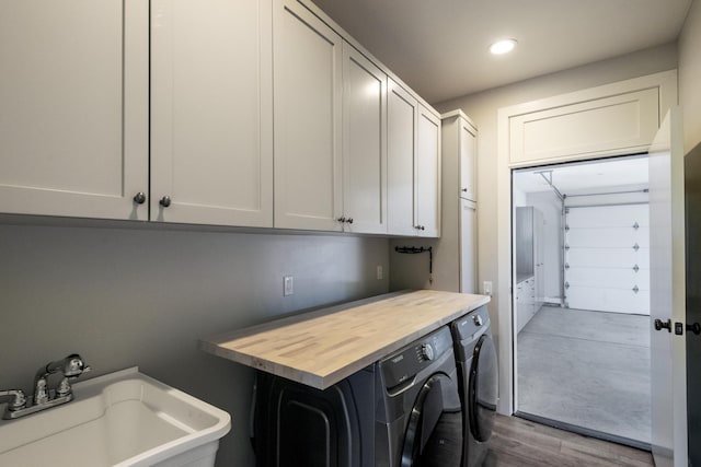 washroom with cabinet space, a sink, wood finished floors, a garage, and independent washer and dryer