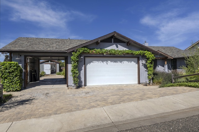 ranch-style house featuring an outbuilding, decorative driveway, stucco siding, a shingled roof, and a garage