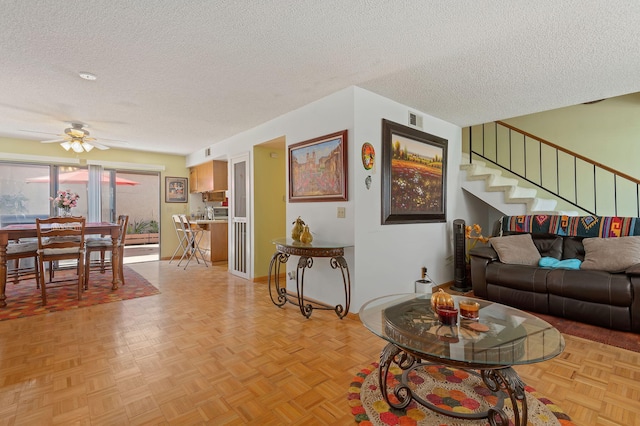 living room featuring light parquet flooring, ceiling fan, and a textured ceiling