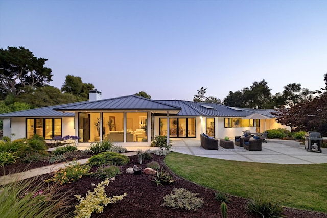 back house at dusk with an outdoor living space, a yard, and a patio area