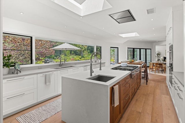 kitchen with sink, an island with sink, white cabinetry, a skylight, and a healthy amount of sunlight