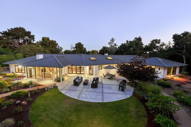 back house at dusk featuring a yard and a patio area