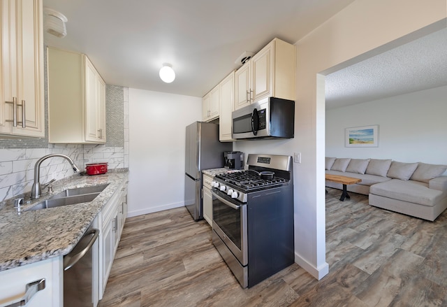 kitchen featuring appliances with stainless steel finishes, light stone countertops, light wood-type flooring, and sink