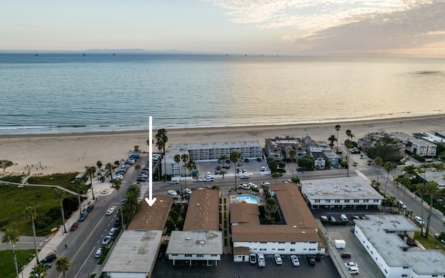 aerial view at dusk featuring a water view and a beach view