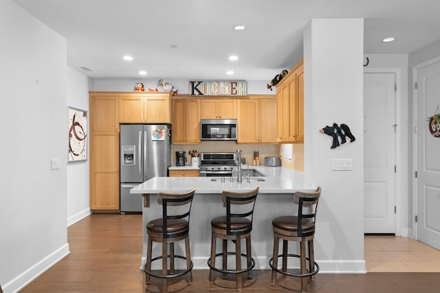 kitchen featuring kitchen peninsula, appliances with stainless steel finishes, hardwood / wood-style floors, and a breakfast bar area