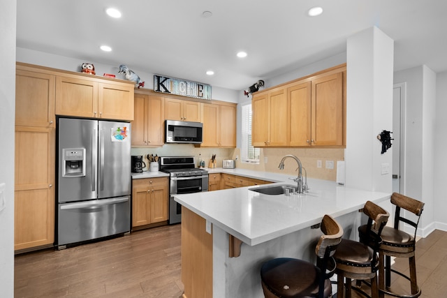 kitchen with sink, stainless steel appliances, light hardwood / wood-style floors, and kitchen peninsula