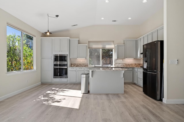 kitchen featuring light stone countertops, light wood finished floors, a kitchen island, freestanding refrigerator, and stainless steel microwave