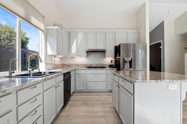 kitchen featuring a sink, cooktop, under cabinet range hood, dishwasher, and stainless steel fridge