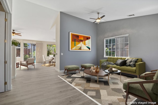 living area with visible vents, baseboards, ceiling fan, light wood-style flooring, and a towering ceiling