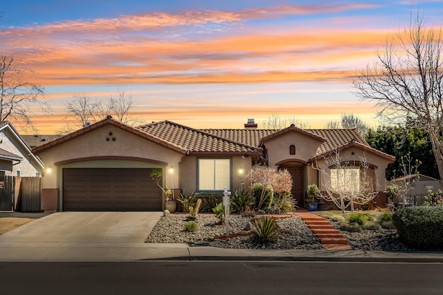 mediterranean / spanish-style house featuring a garage, stucco siding, driveway, and fence