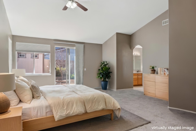 bedroom with visible vents, lofted ceiling, light carpet, ensuite bathroom, and arched walkways