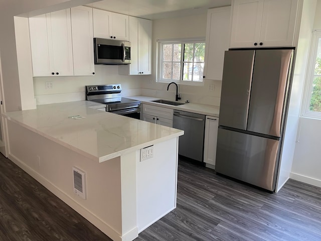 kitchen with light stone counters, stainless steel appliances, kitchen peninsula, and white cabinetry