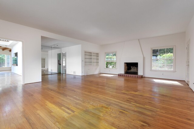 unfurnished living room featuring built in features, wood-type flooring, a brick fireplace, and plenty of natural light