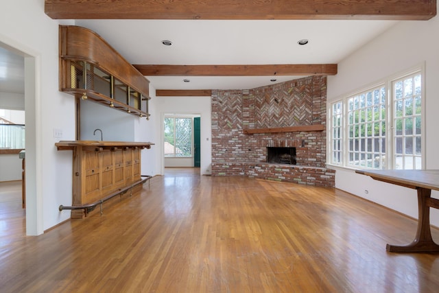 unfurnished living room featuring beamed ceiling, a brick fireplace, and hardwood / wood-style flooring