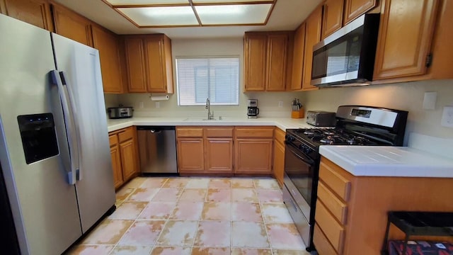 kitchen featuring stainless steel appliances, brown cabinetry, light countertops, and a sink