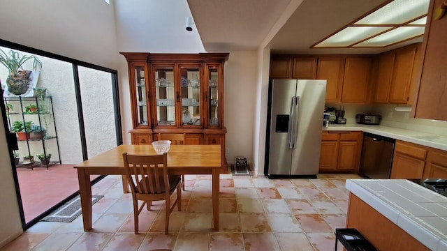 kitchen featuring tile countertops, dishwashing machine, stainless steel fridge, and brown cabinetry