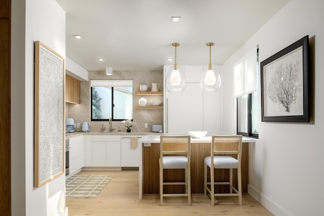 kitchen featuring white cabinets, decorative backsplash, light hardwood / wood-style floors, and hanging light fixtures