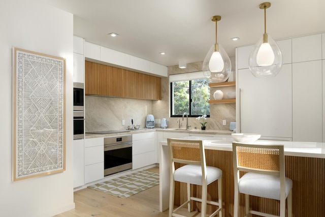 kitchen with stainless steel oven, sink, decorative backsplash, decorative light fixtures, and white cabinetry