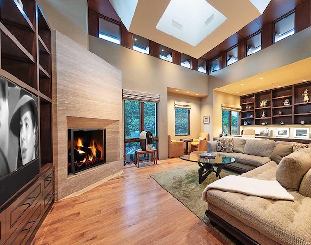 living room with built in features, light wood-type flooring, a large fireplace, and a towering ceiling