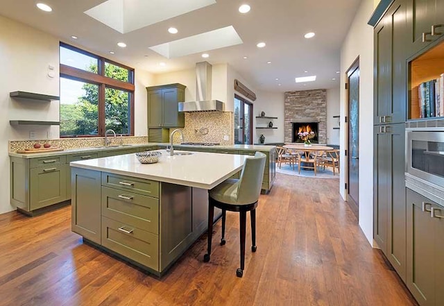 kitchen featuring wall chimney exhaust hood, a kitchen breakfast bar, dark wood-type flooring, green cabinets, and an island with sink