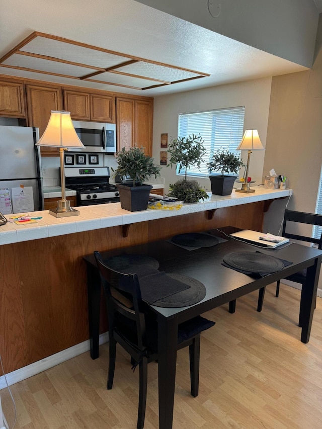 kitchen featuring a kitchen breakfast bar, light wood-type flooring, appliances with stainless steel finishes, tile counters, and kitchen peninsula