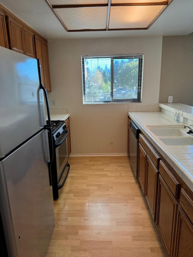 kitchen featuring tile countertops, light hardwood / wood-style floors, sink, and appliances with stainless steel finishes