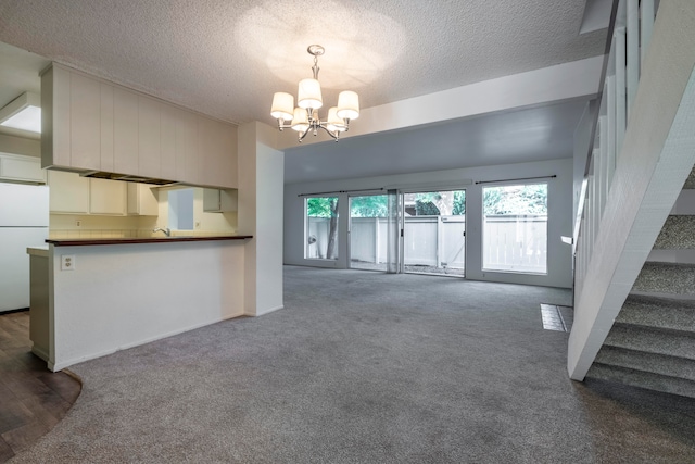 unfurnished living room with dark carpet, an inviting chandelier, and a textured ceiling