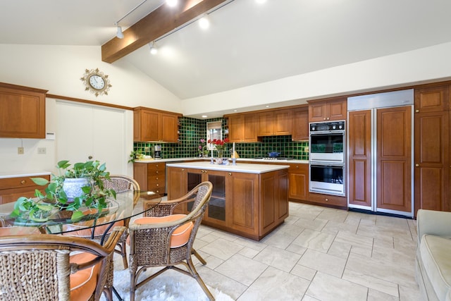 kitchen with backsplash, track lighting, stainless steel double oven, a kitchen island with sink, and paneled built in refrigerator