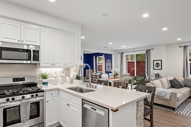 kitchen featuring kitchen peninsula, sink, white cabinets, light wood-type flooring, and appliances with stainless steel finishes