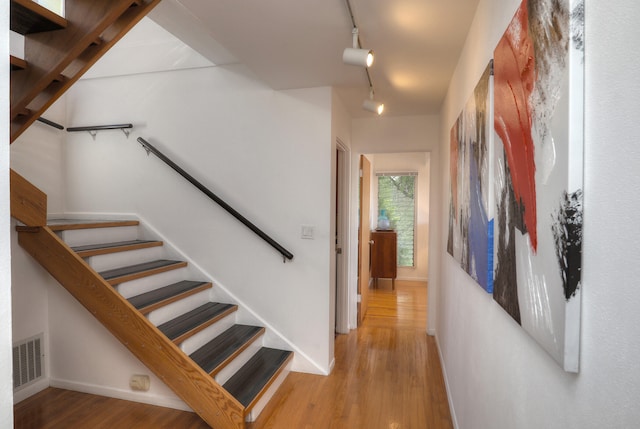 staircase featuring baseboards, track lighting, visible vents, and wood finished floors