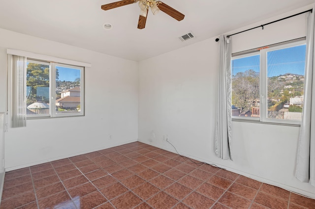 unfurnished room with dark tile patterned flooring, a wealth of natural light, and ceiling fan