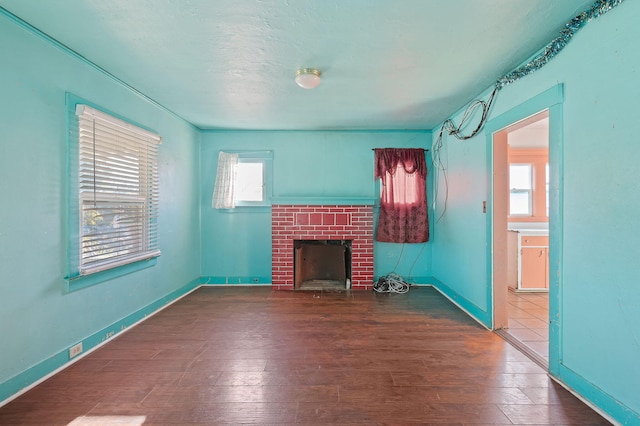 unfurnished living room featuring a brick fireplace, dark wood-type flooring, and a textured ceiling