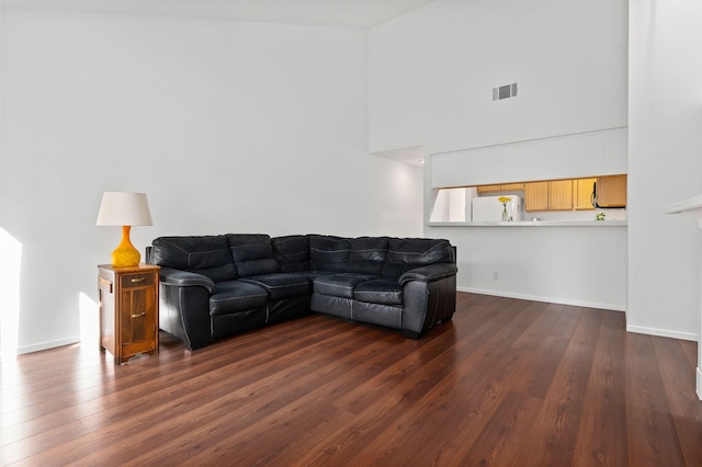 living room featuring a towering ceiling and dark wood-type flooring