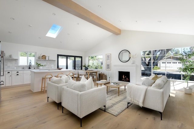 living room featuring beamed ceiling, sink, light wood-type flooring, high vaulted ceiling, and a skylight