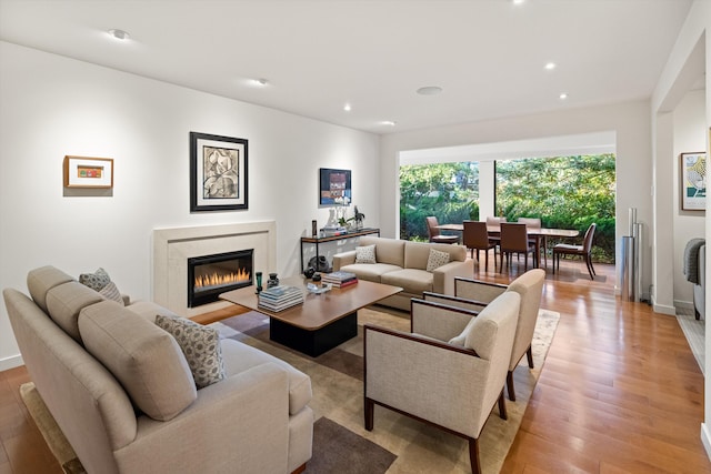 living area featuring light wood-type flooring, a glass covered fireplace, baseboards, and recessed lighting