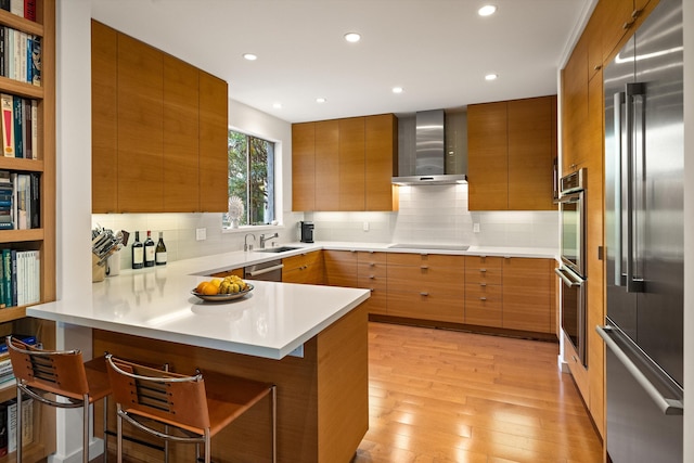 kitchen featuring kitchen peninsula, appliances with stainless steel finishes, a breakfast bar area, wall chimney range hood, and light wood-type flooring