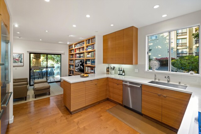 kitchen featuring stainless steel dishwasher, kitchen peninsula, sink, and light wood-type flooring